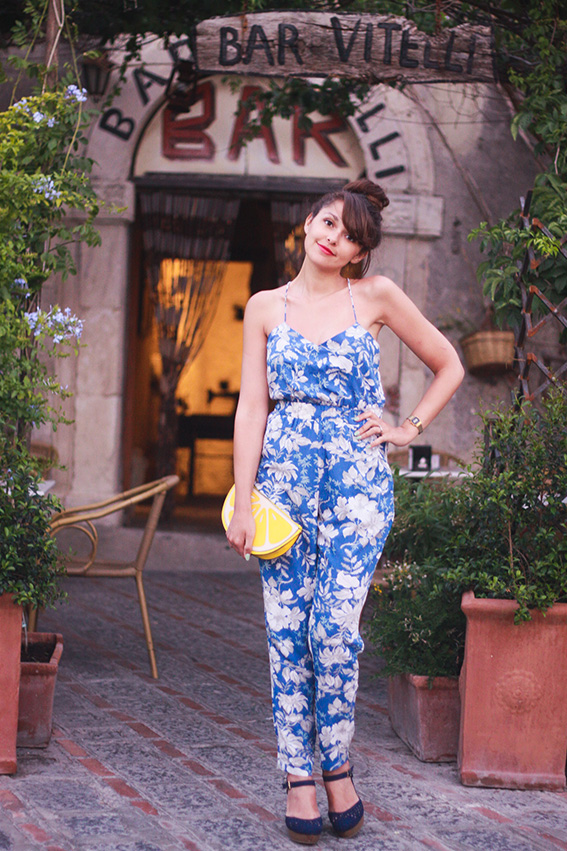 Bar Vitelli, Savoca en Sicile, bar où une scène du Parrain a été tournée: combinaison fleurie tropicale bleue et blanche, chaussures compensées et pochette Newlook en forme de citron